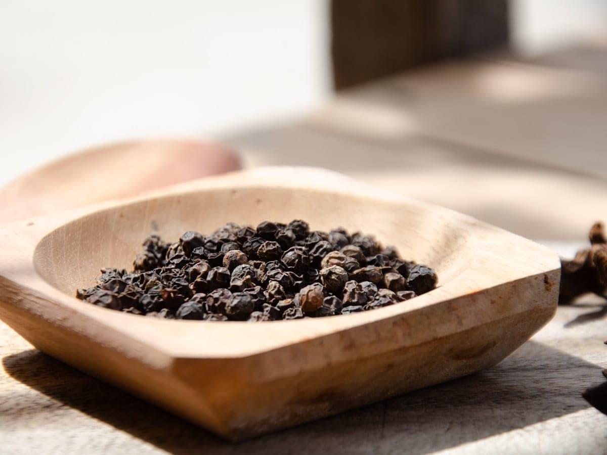 Black peppercorns heaped in a carved wooden bowl