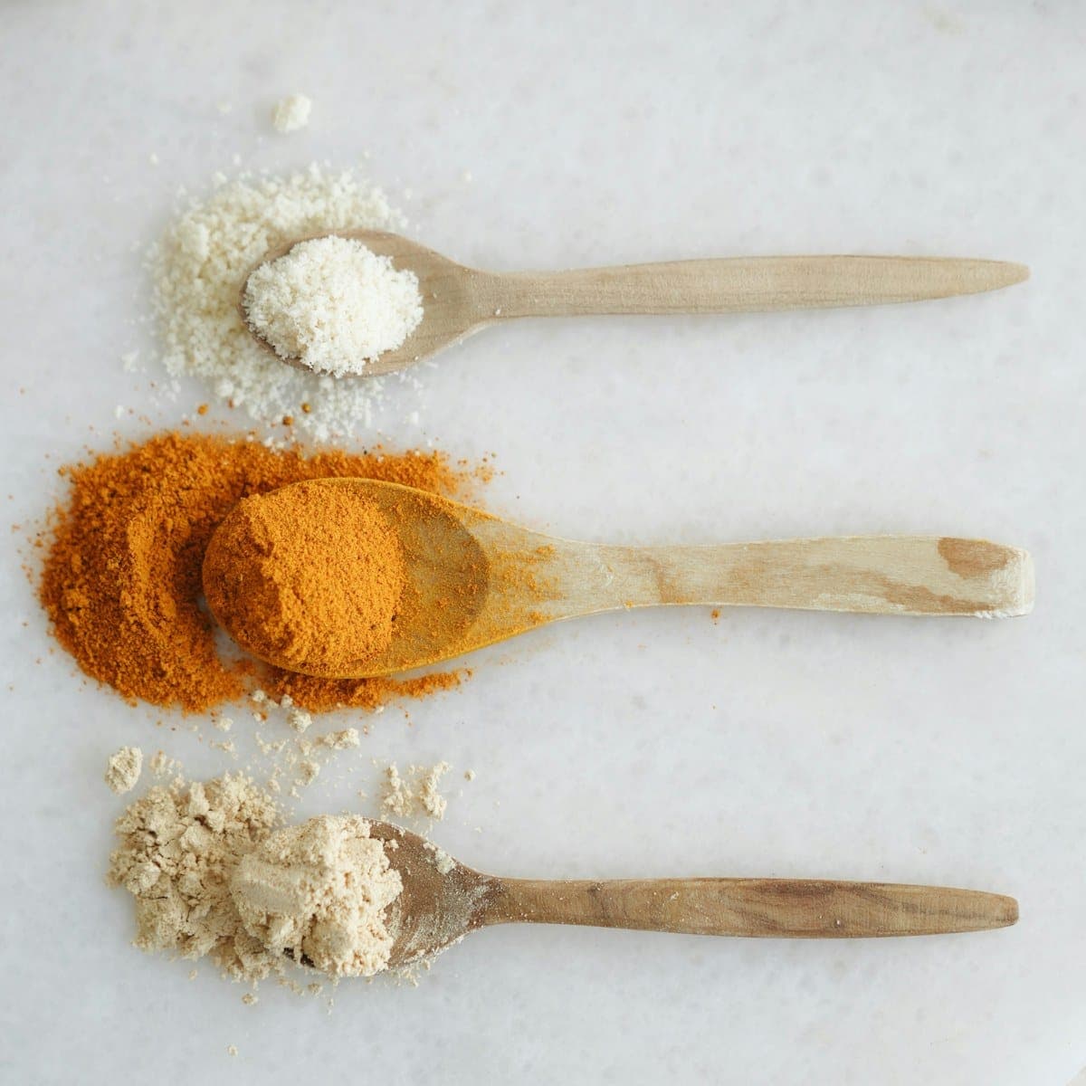Three wooden spoons holding paprika, smoked salt, and garlic powder