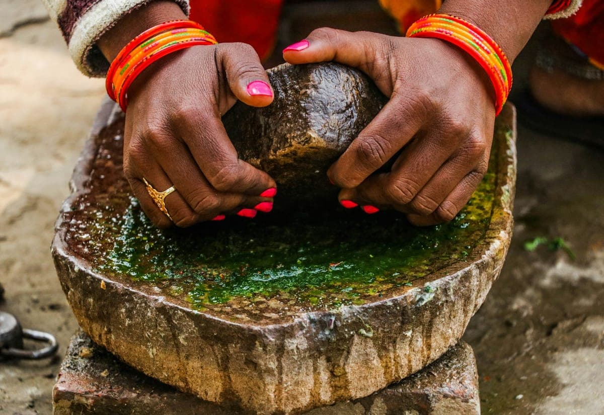 Two hands working a stone mortar full of spices