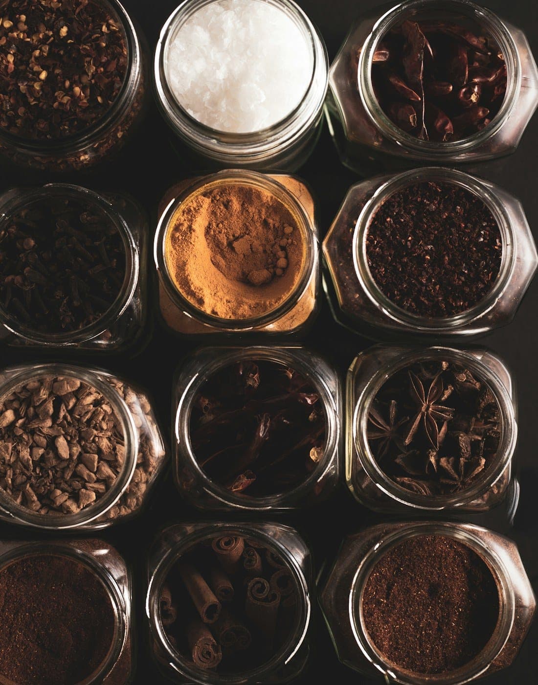 Jars of house spice blends seen from above on a dark counter